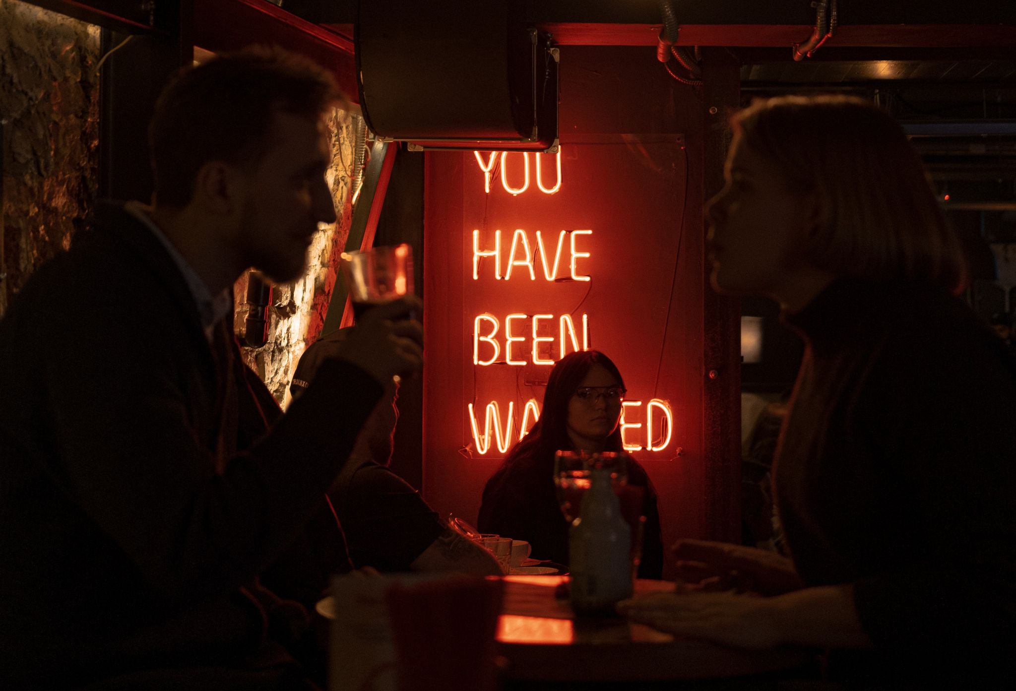 Photo by Alexandra Patrusheva - Adult couple talking and enjoying bar with bright neon signboard